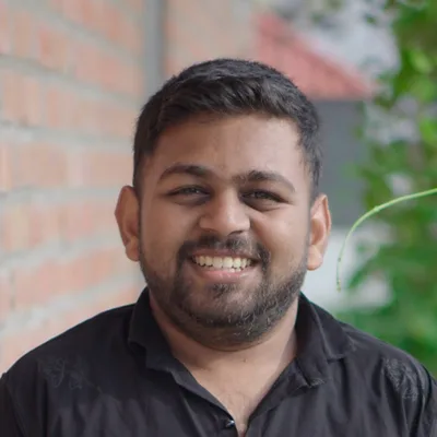 Sanju K S smiling outdoors beside a brick wall